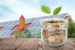 Háztető napelemekkel és távolabb egy befőttes üveg tele aprópénzel