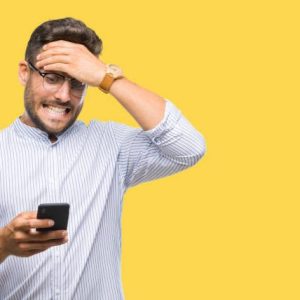 Young handsome man texting using smartphone over isolated background stressed with hand on head, shocked with shame and surprise face, angry and frustrated. Fear and upset for mistake.